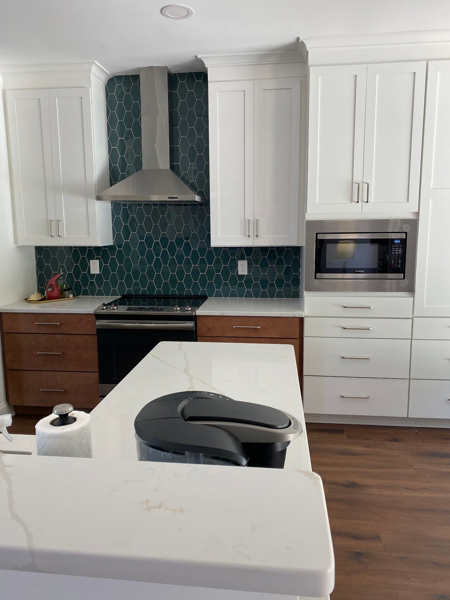 Modern kitchen with white cabinets, dark teal backsplash, stainless steel appliances, and white countertop.