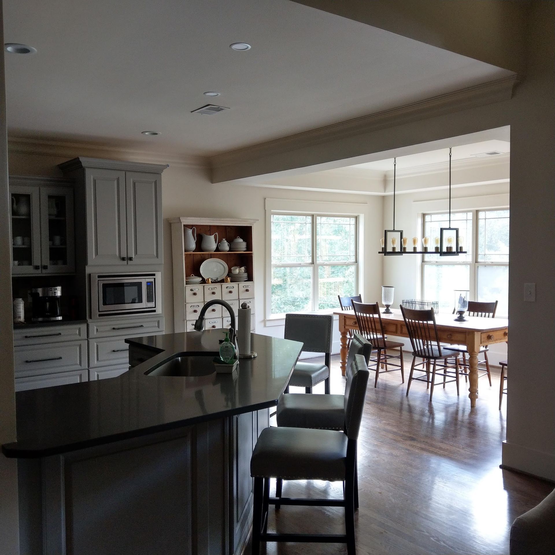Kitchen with gray cabinets, island, and open dining area with wooden table and chairs.