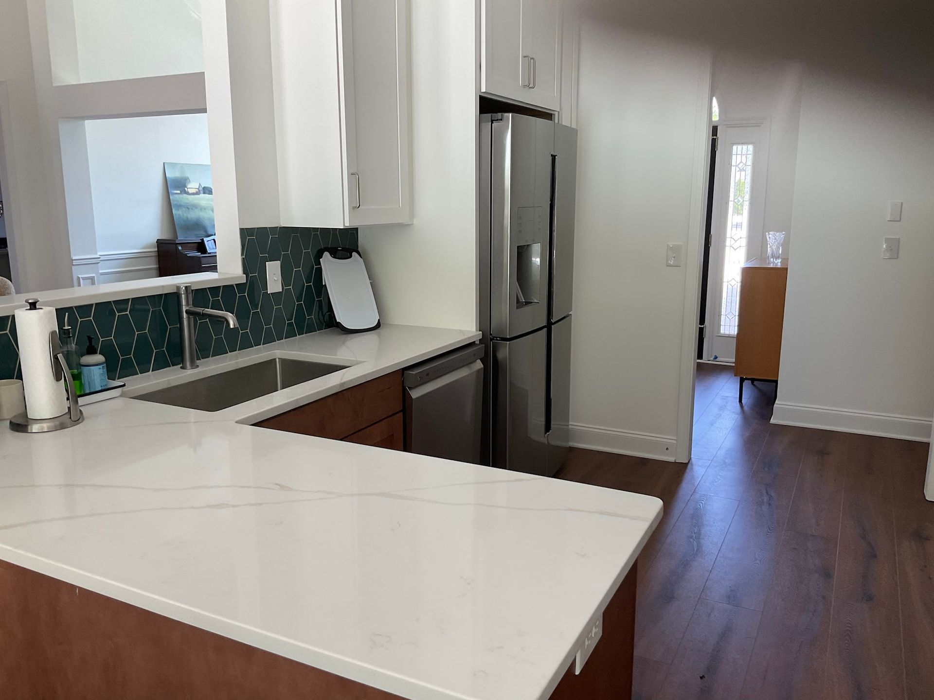 Modern kitchen with white countertop, stainless steel refrigerator, and teal tile backsplash.
