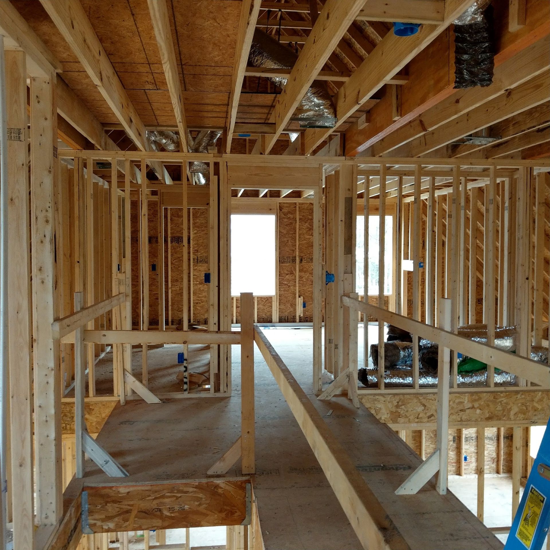 Interior view of a wooden house under construction. Stud framing, exposed beams, unfinished walls, and a hallway.