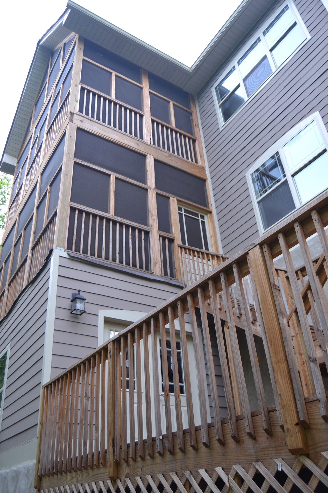 Screened-in porch on a house with a wooden deck and siding, brown screens and trim.