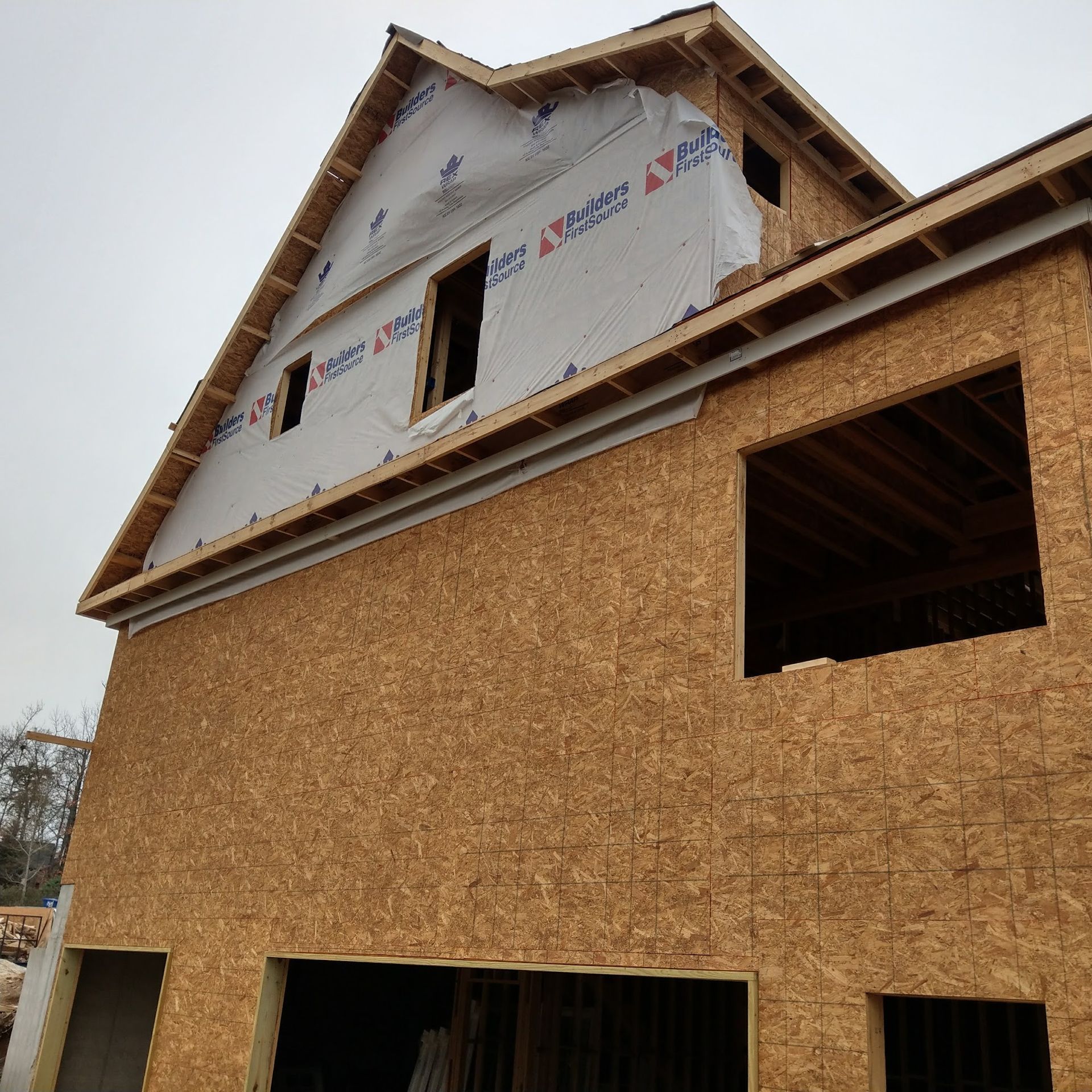 Construction of a two-story building with a gable roof, covered in sheathing, with open window and door frames.