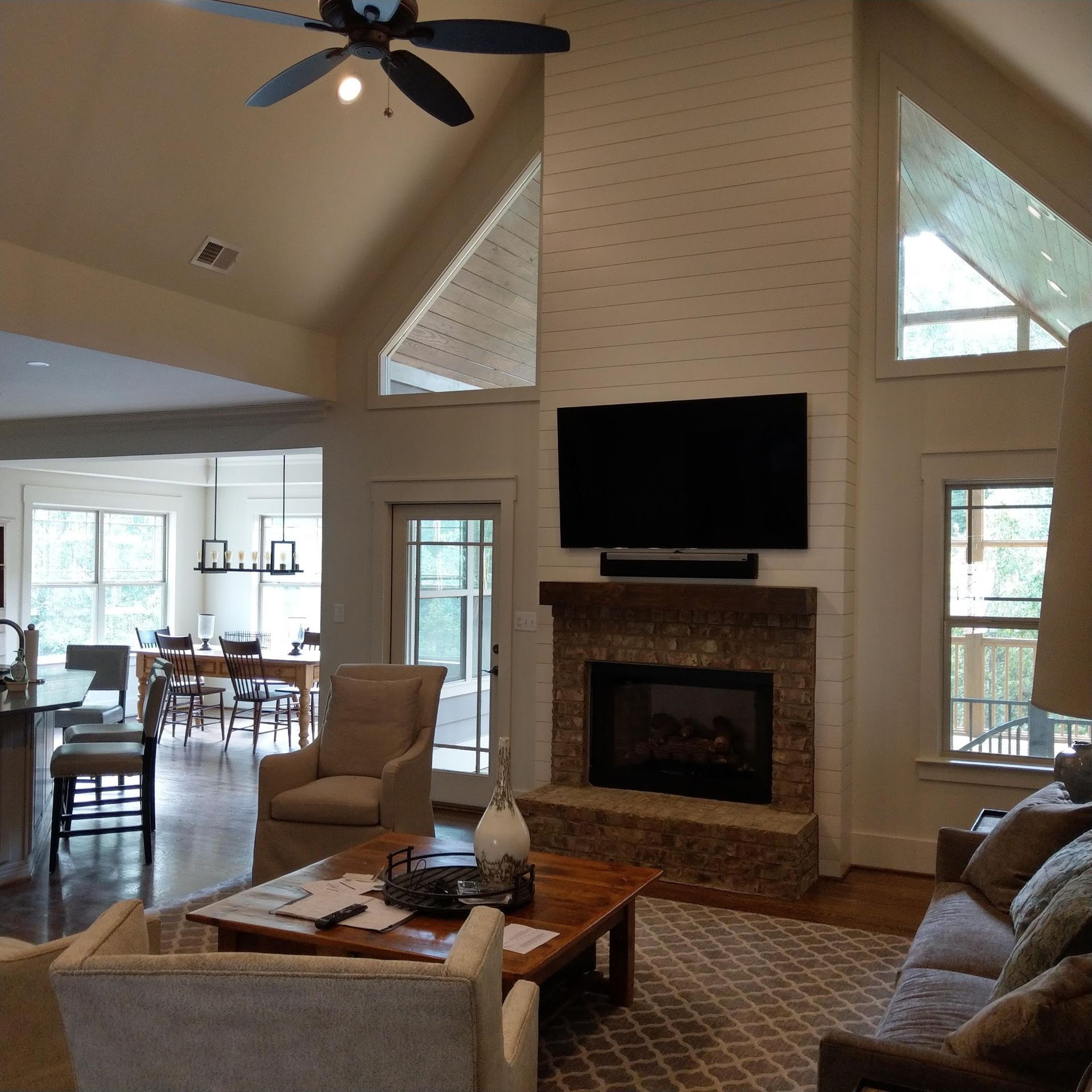 Living room with fireplace, TV, vaulted ceiling, windows, and open view to dining area.