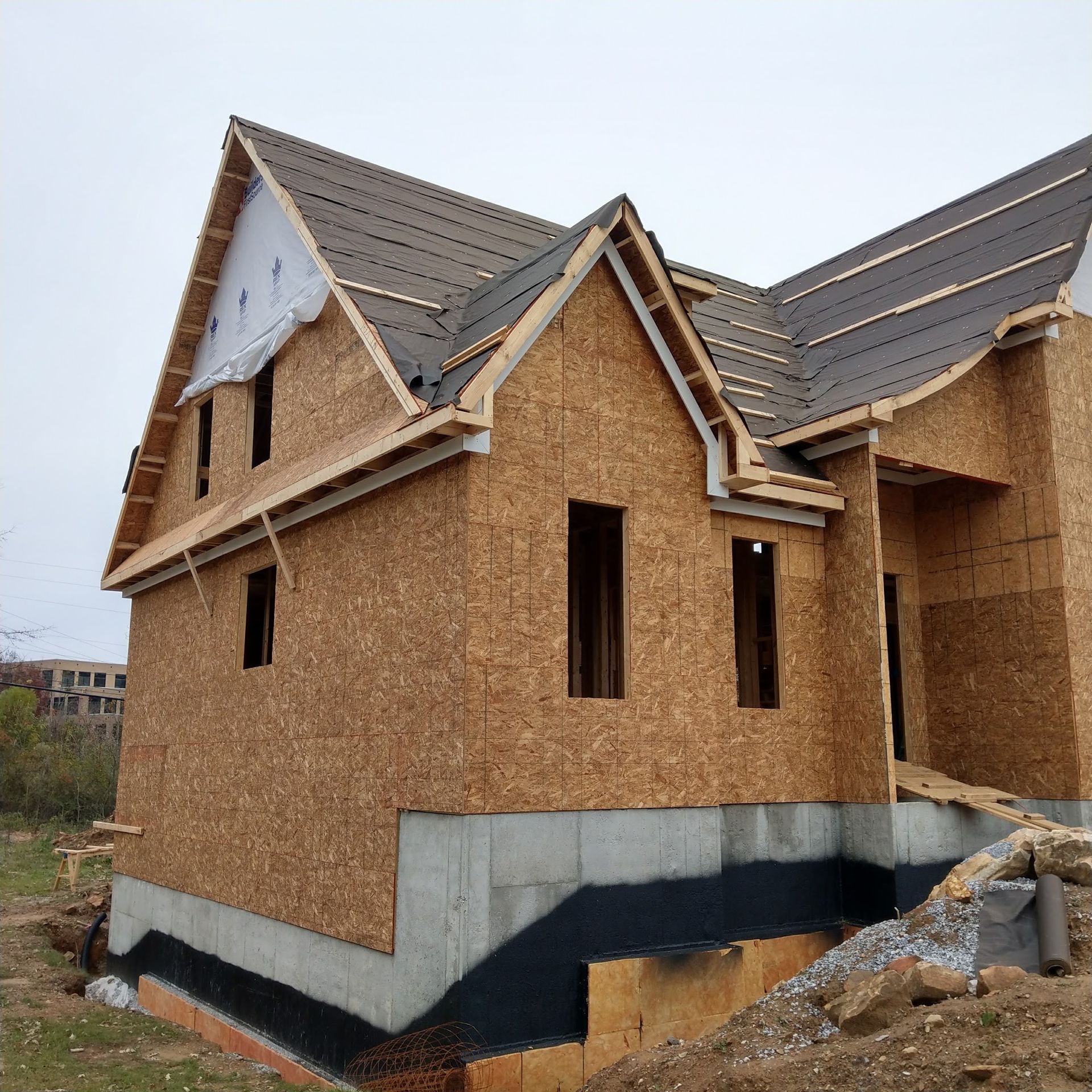 Construction of a two-story house, featuring OSB sheathing and partial roofing. Foundation visible.