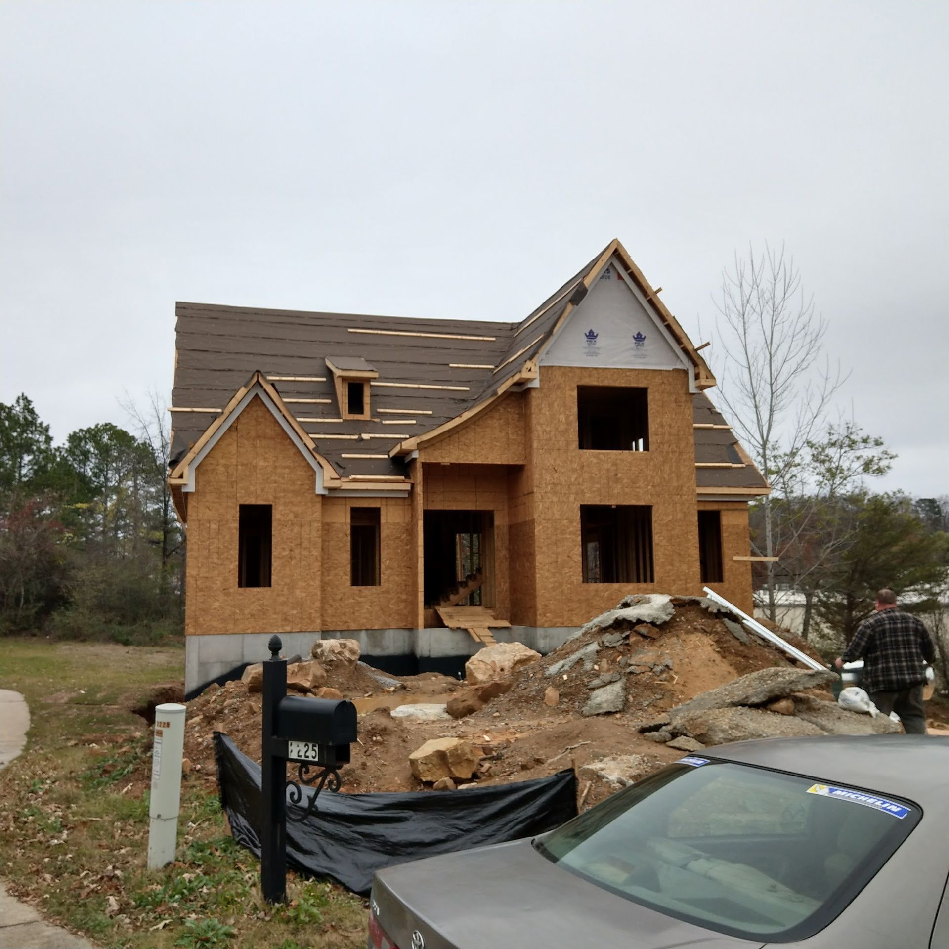 House under construction with exposed framing and a person walking nearby.