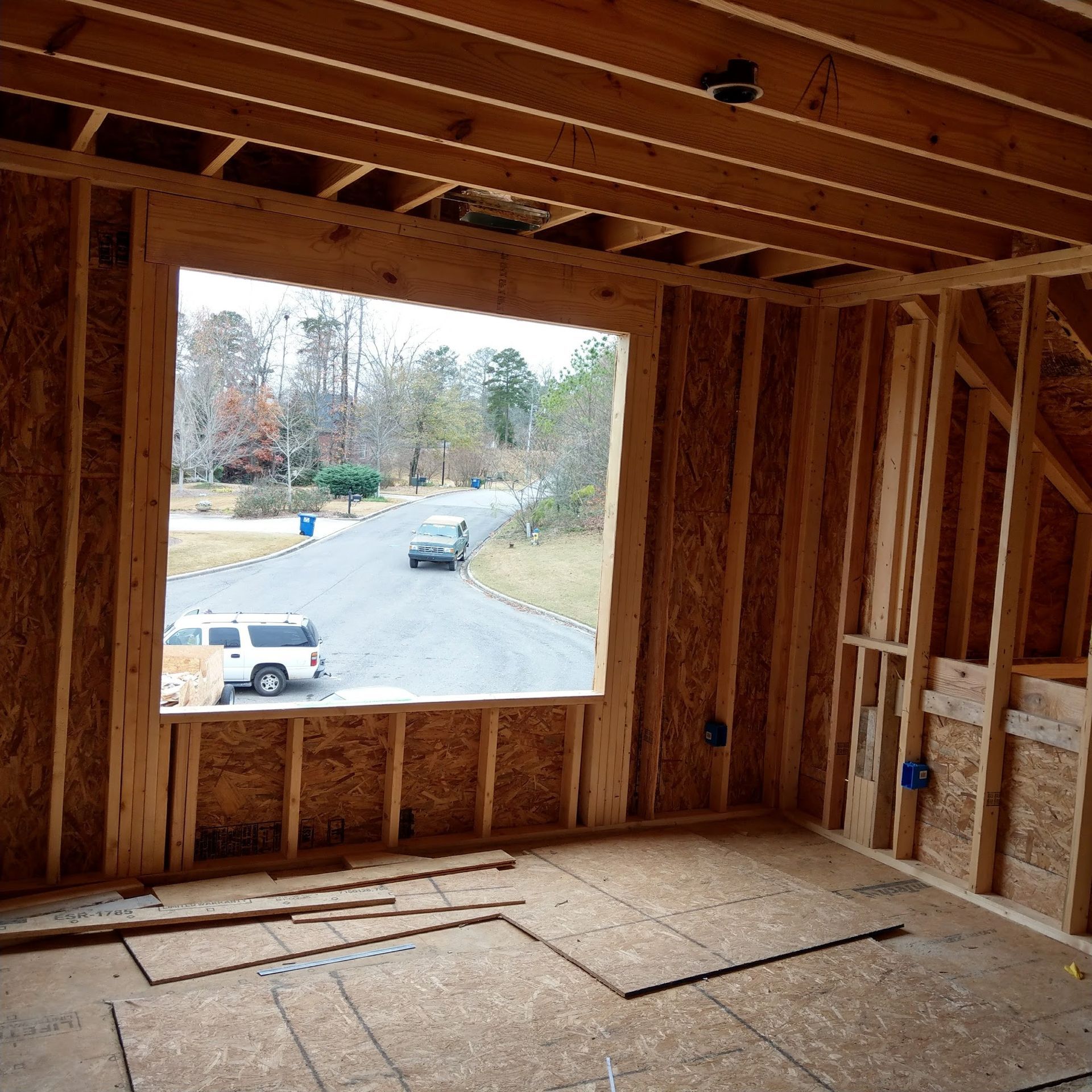 Interior view of a building under construction, framed with wooden beams; a window offers a view of a street.