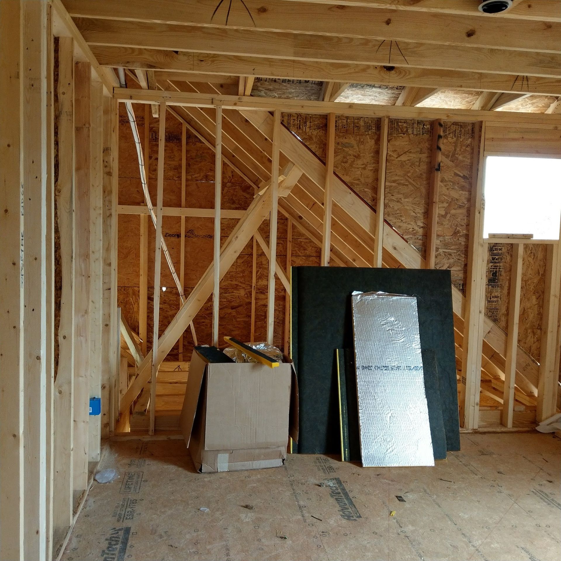 Interior of a wood-framed room under construction with exposed beams, insulation, and tools.