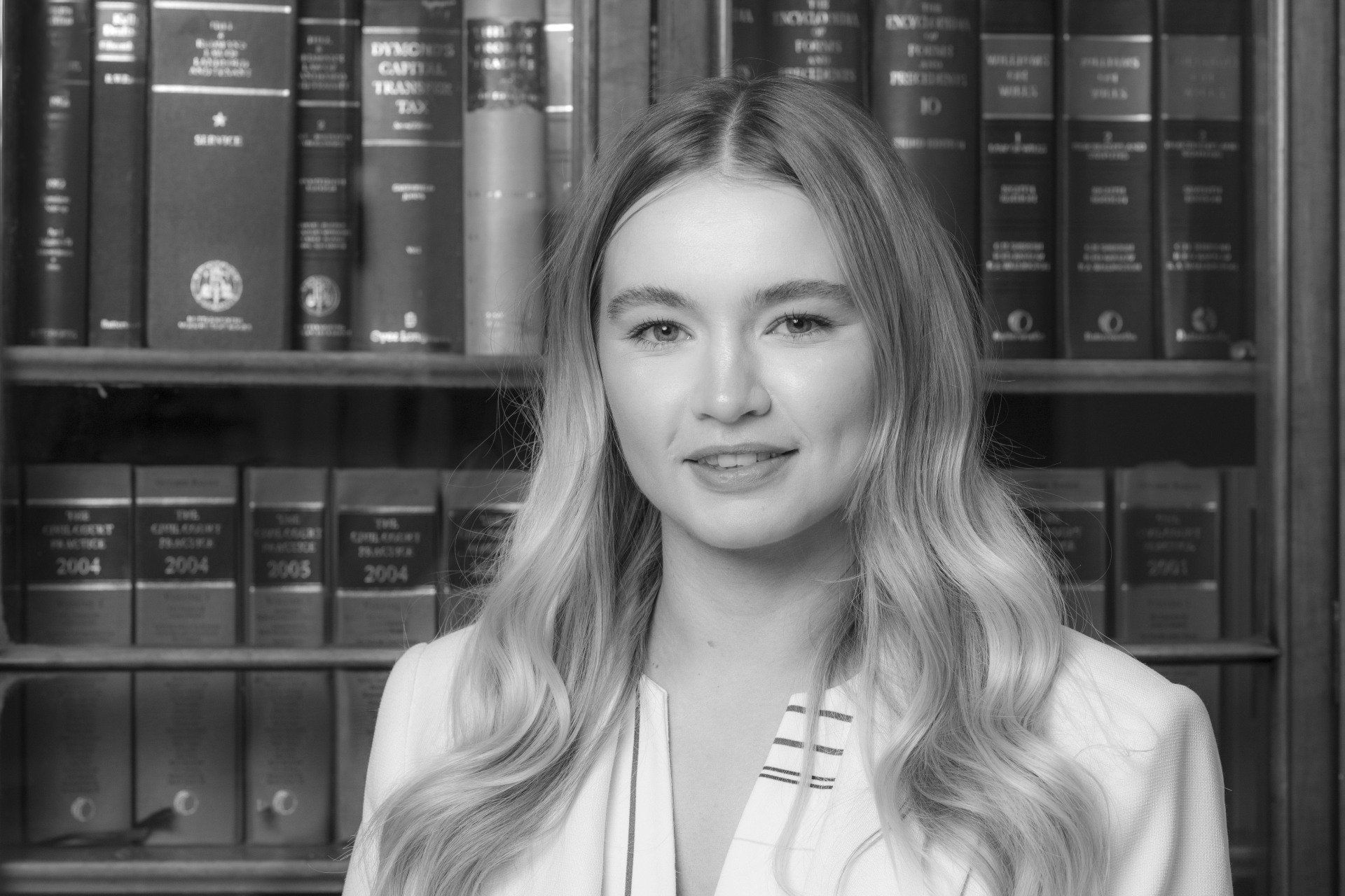 Woman standing in front of bookshelves in a library, smiling at the camera.