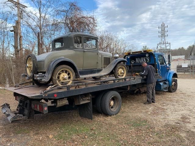 An old car is being towed by a tow truck.