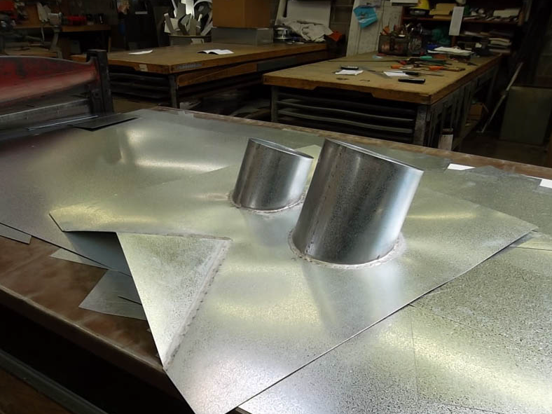 Metal roof flashing sheets with two silver vent pipes on a workbench in a workshop