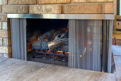 Brick fireplace with burning logs and a metal mesh screen inside a hearth
