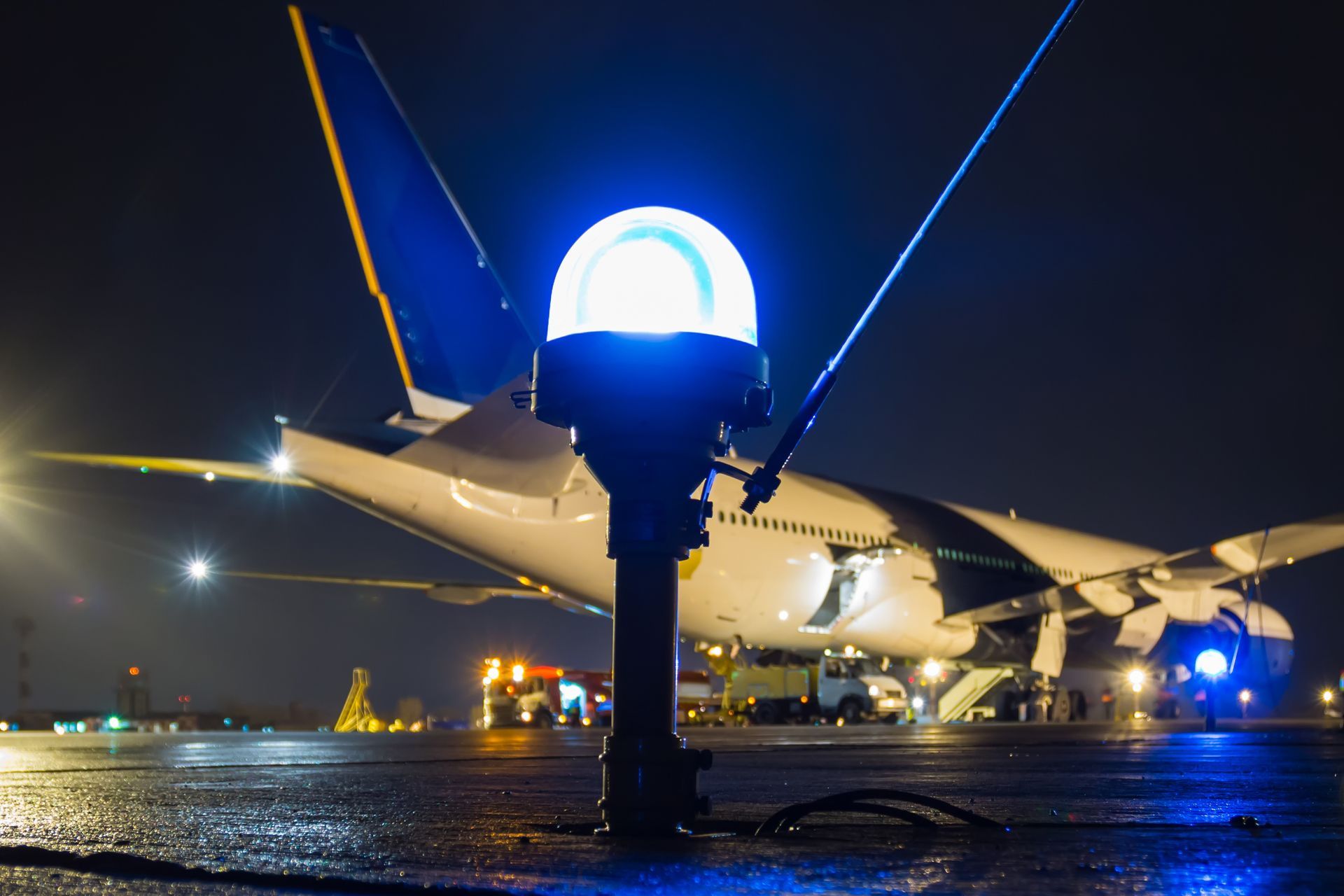 A close-up of a taxiway side row light in the foreground of a large passenger aircraft at night. A close-up of a taxiway side row light in the foreground of a large passenger aircraft at night.