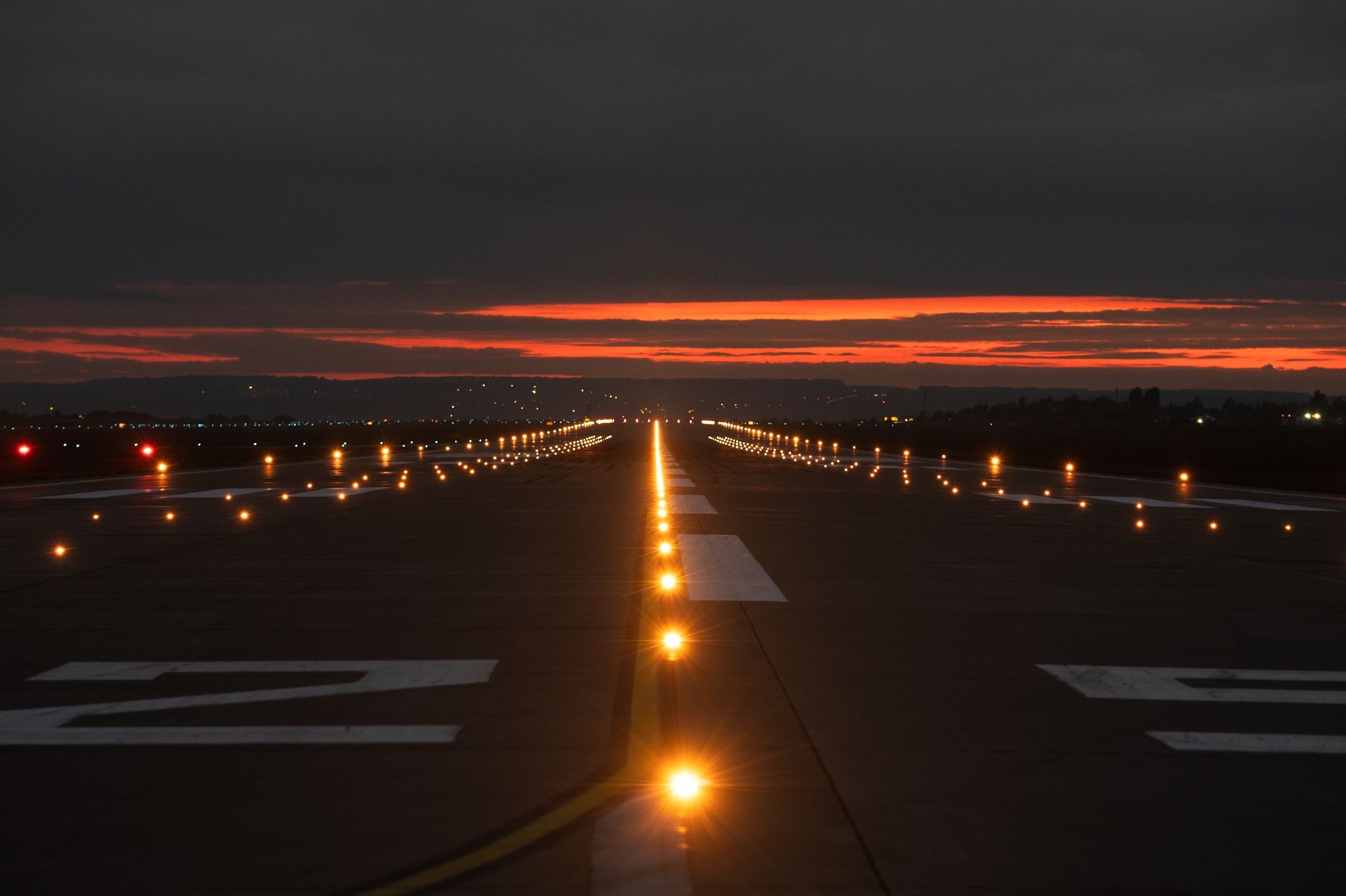 An airport runway illuminated by lights during a vibrant sunset