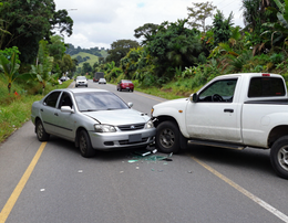 Dos coches chocan frontalmente en una carretera, quedando restos esparcidos entre ellos.
