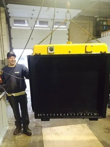 Worker standing beside a large suspended yellow-and-black industrial container in a workshop