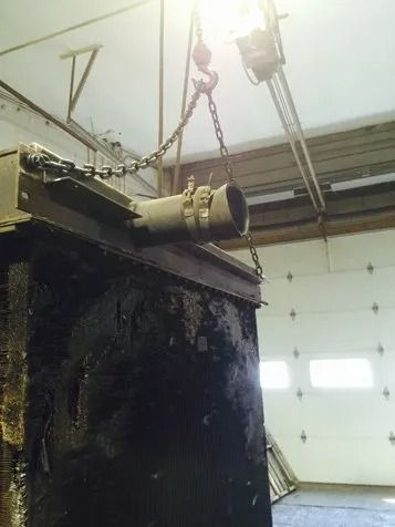 Industrial tank hanging from chains in a warehouse, with a garage-style door in the background.