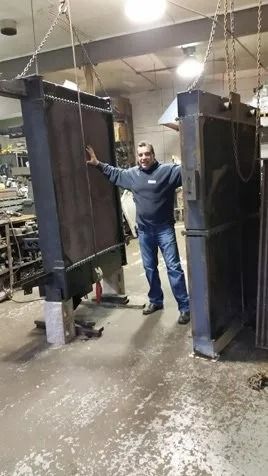 Man in blue coveralls standing between hanging black panels in a workshop