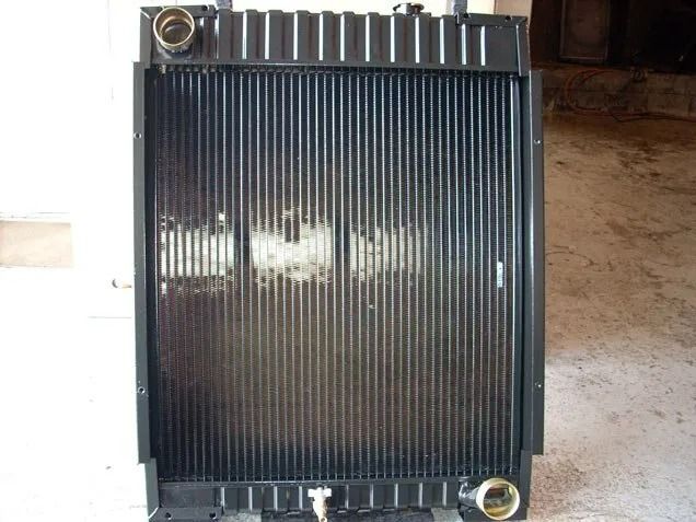 Black radiator with metal fittings on top and bottom, shown against a garage floor.