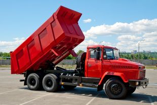 Red dump truck with raised bed on a paved lot under a blue sky Red dump truck with raised bed on a paved lot under a blue sky