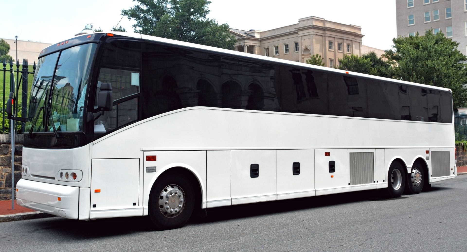 White luxury coach bus parked on a street with buildings in the background