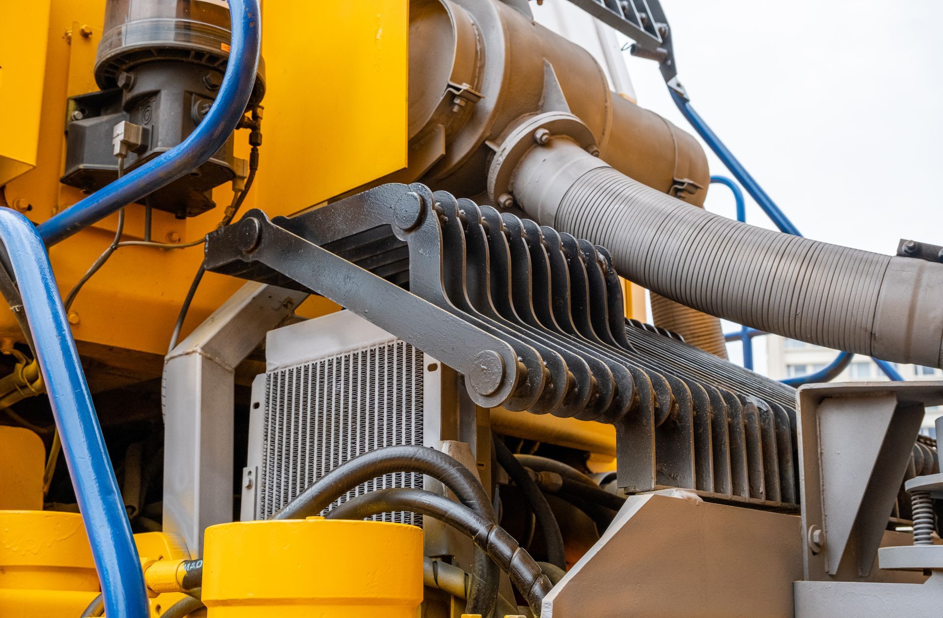 Close-up of industrial machinery with yellow metal parts, hoses, and a large gray pipe.