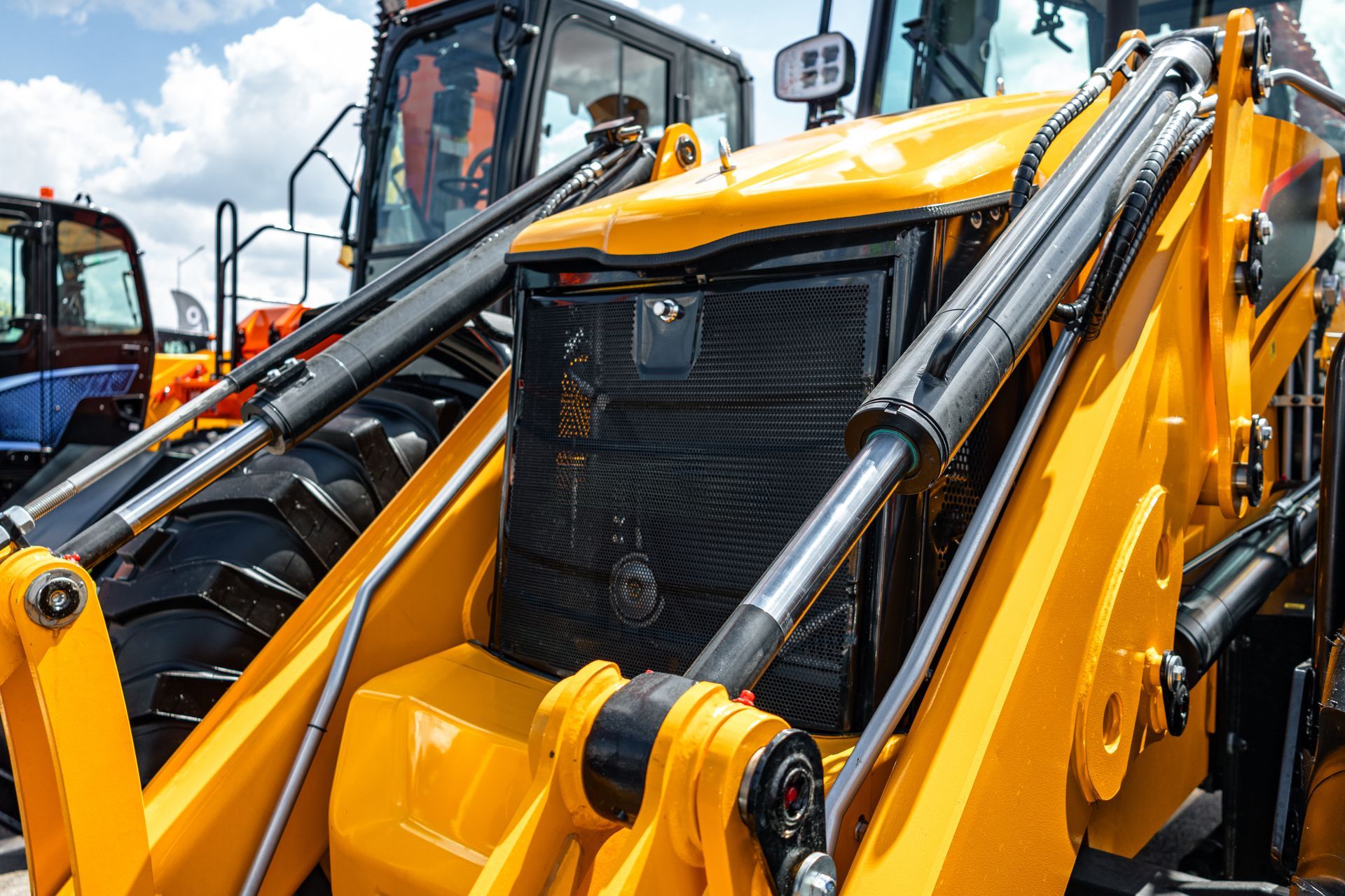 Yellow backhoe loader parked outdoors, with front bucket and hydraulic arms visible close up