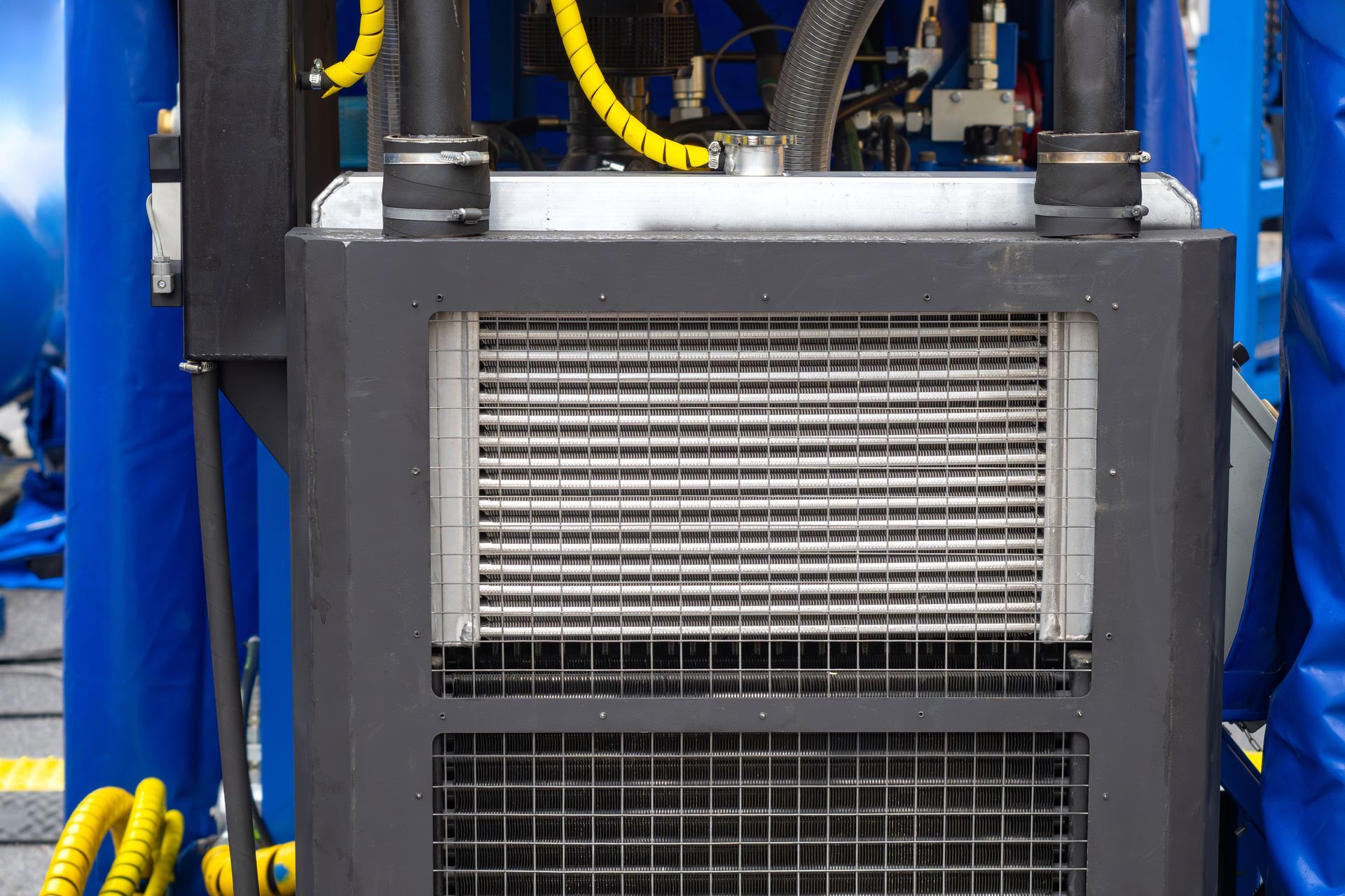 Close-up of gray industrial machine with vented panel, black hoses, and yellow cables against a blue background Close-up of gray industrial machine with vented panel, black hoses, and yellow cables against a blue background