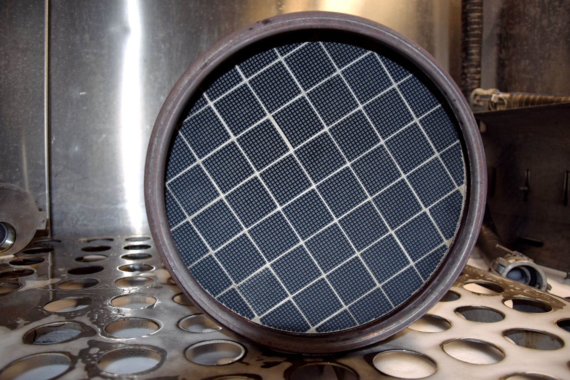 Round diesel particulate filters with dark blue grid pattern, sitting on a perforated metal surface indoors