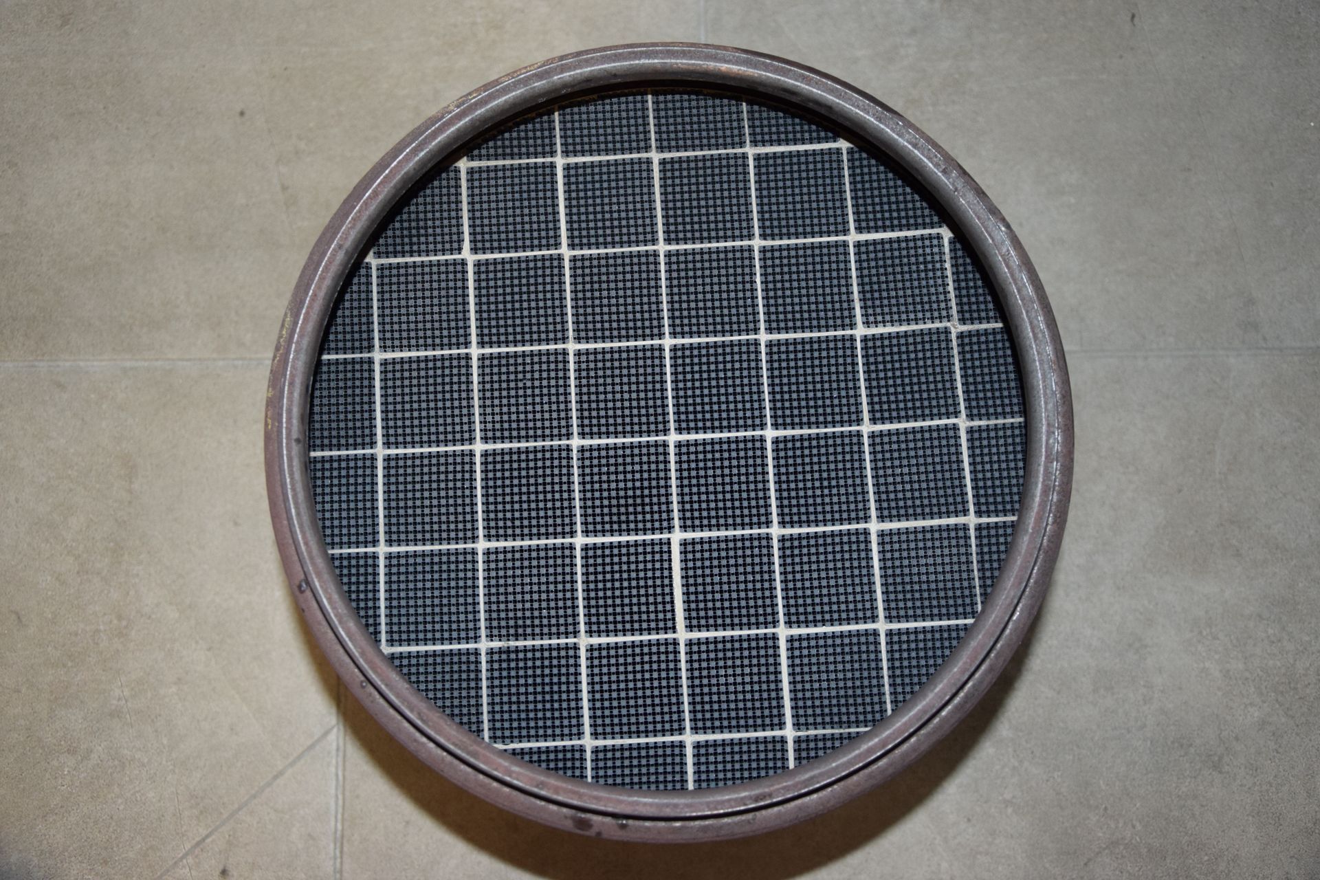 Round black mesh filter with a white grid pattern on a beige surface Round black mesh filter with a white grid pattern on a beige surface