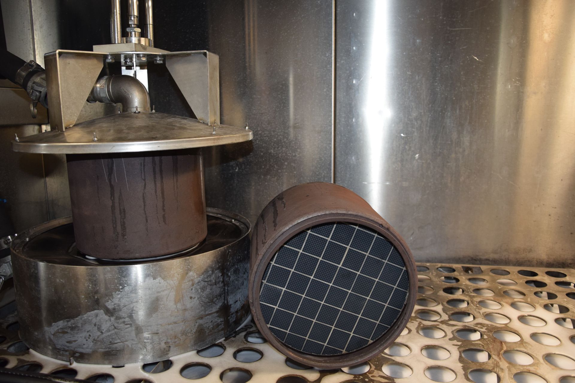 Two brown cylindrical filters beside a perforated metal surface inside industrial equipment. Two brown cylindrical filters beside a perforated metal surface inside industrial equipment.