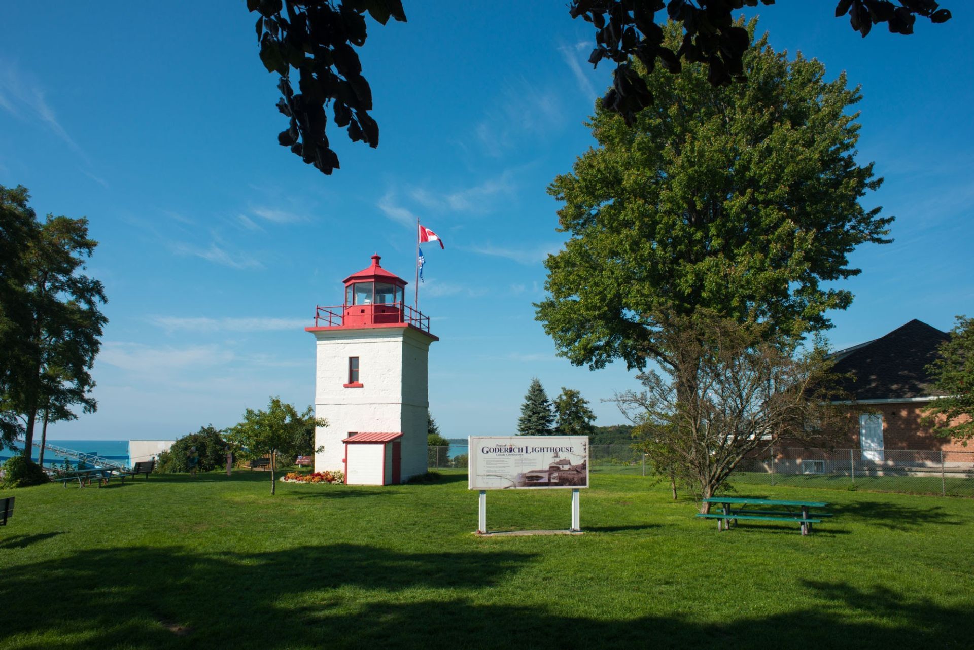 White lighthouse with red roof on a grassy park under a clear blue sky.