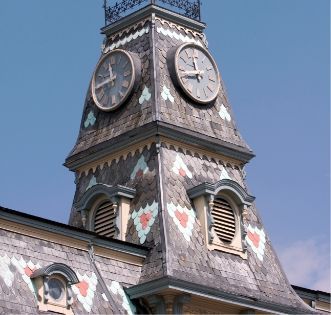 Clock tower with four faces, decorated in pastel heart patterns against a blue sky