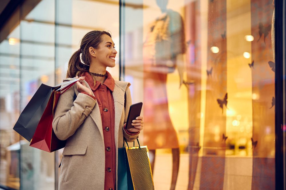 Smiling shopper in blue sunglasses holding colorful shopping bags outdoors