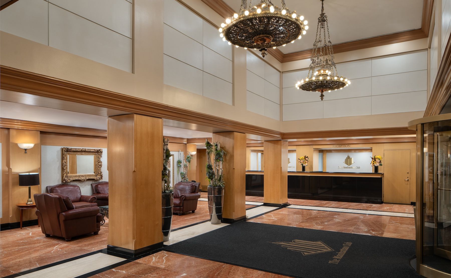 Spacious hotel lobby with chandeliers, wood columns, leather seating, and a reception desk