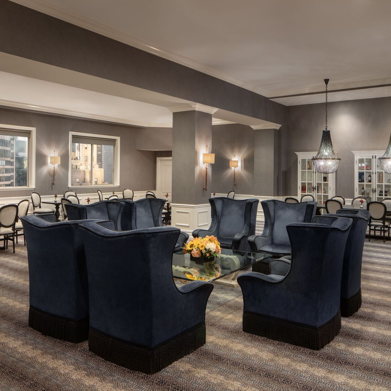 Lounge area with blue armchairs around a glass table, and a dining area in the background.