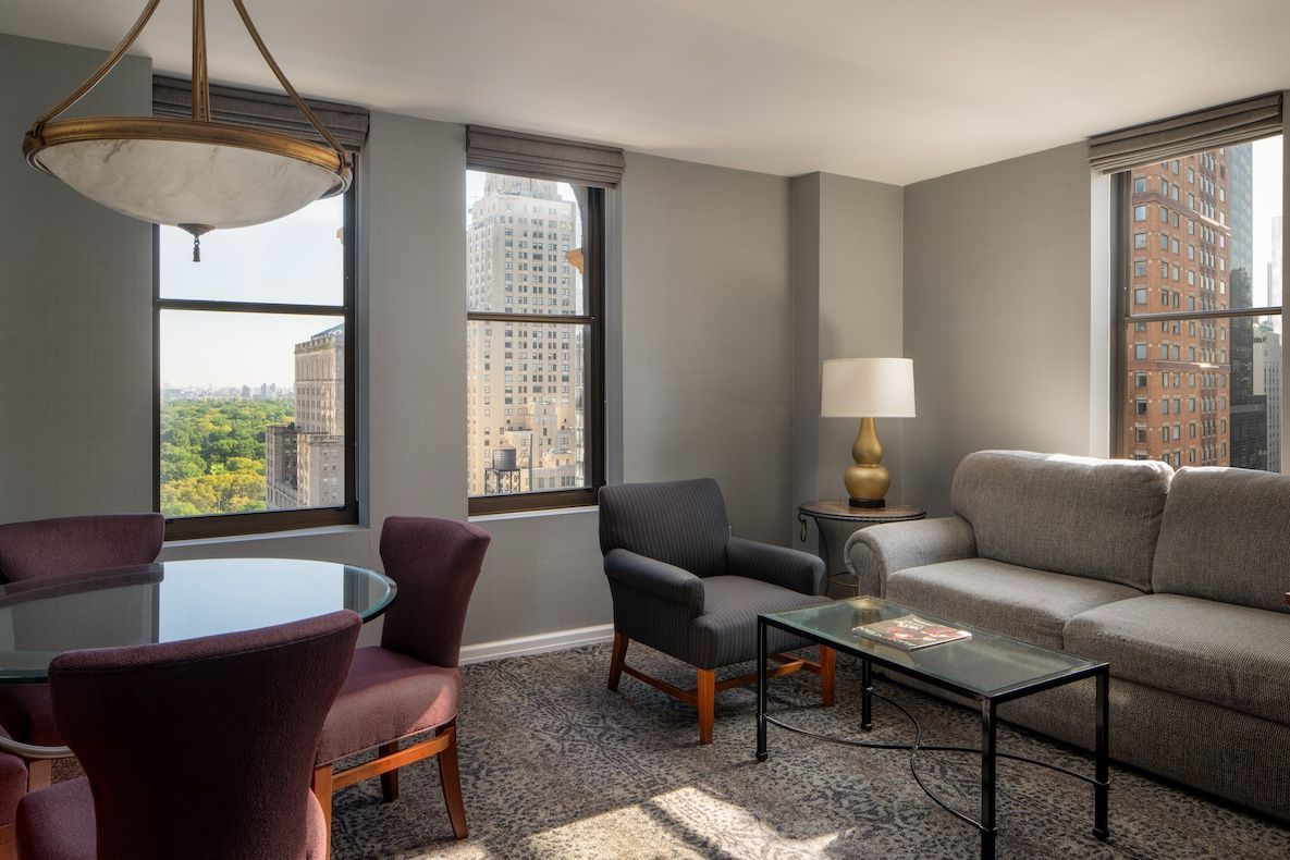 Living room with cityscape view, featuring a sofa, armchair, dining set, and table lamp.