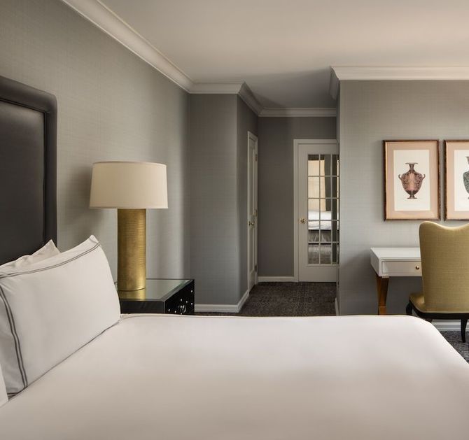Bedroom with a white bed, gold lamp, white desk, and two framed prints on the wall.