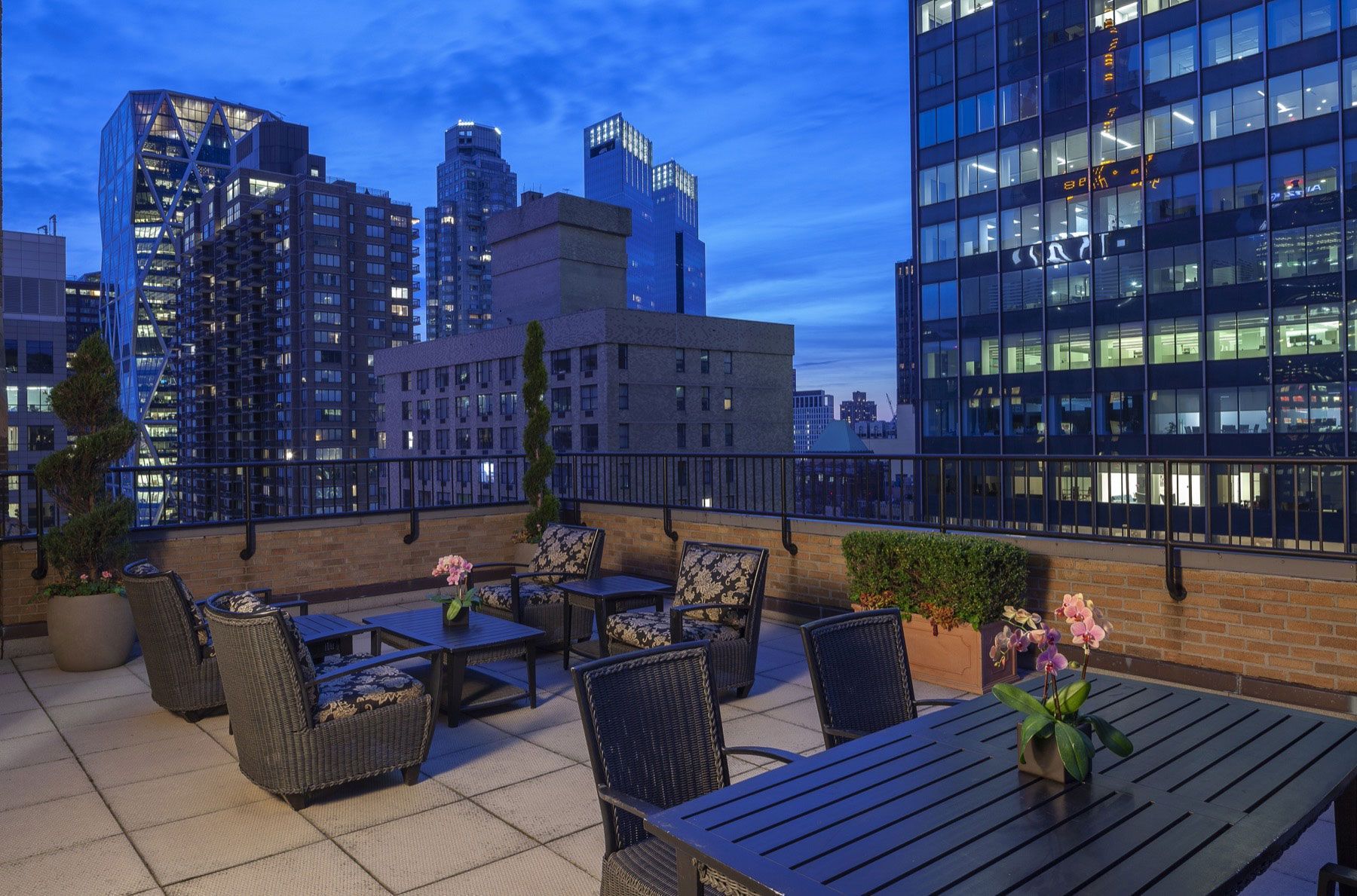 A rooftop patio with outdoor seating and a city skyline view at dusk.