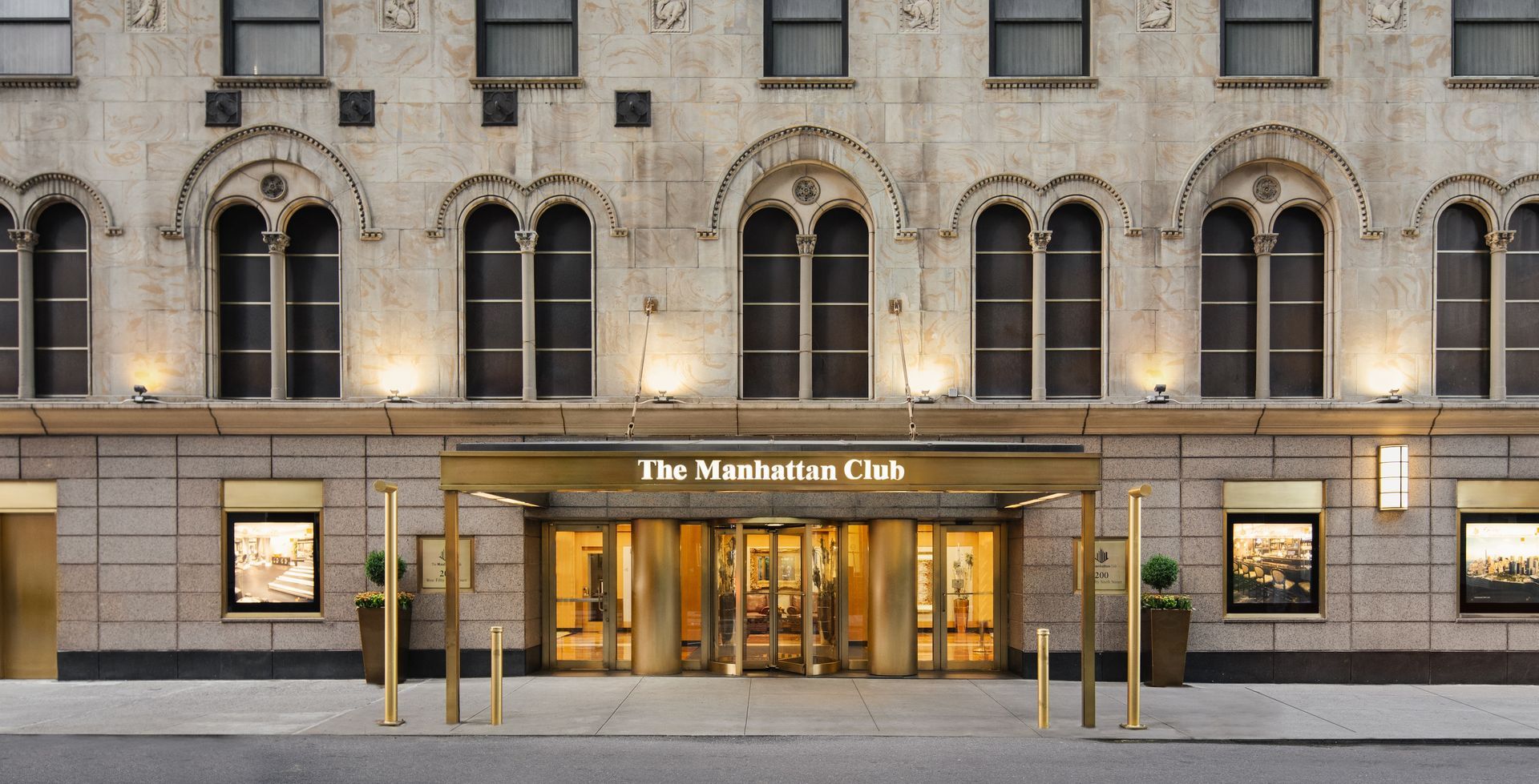 Front entrance of The Macallum Club with stone facade, arched windows, and lit glass doors at dusk