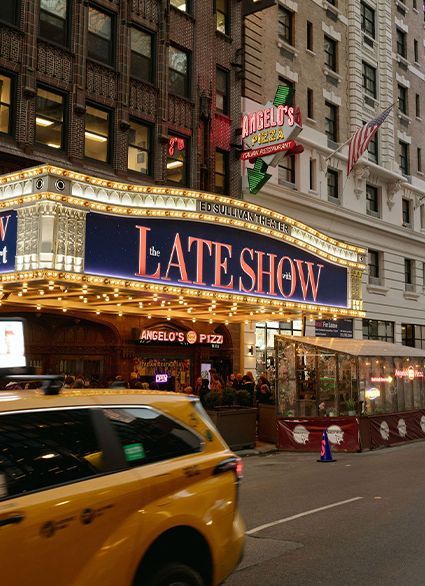 The Late Show marquee outside a city theater at dusk, with a yellow taxi passing by.