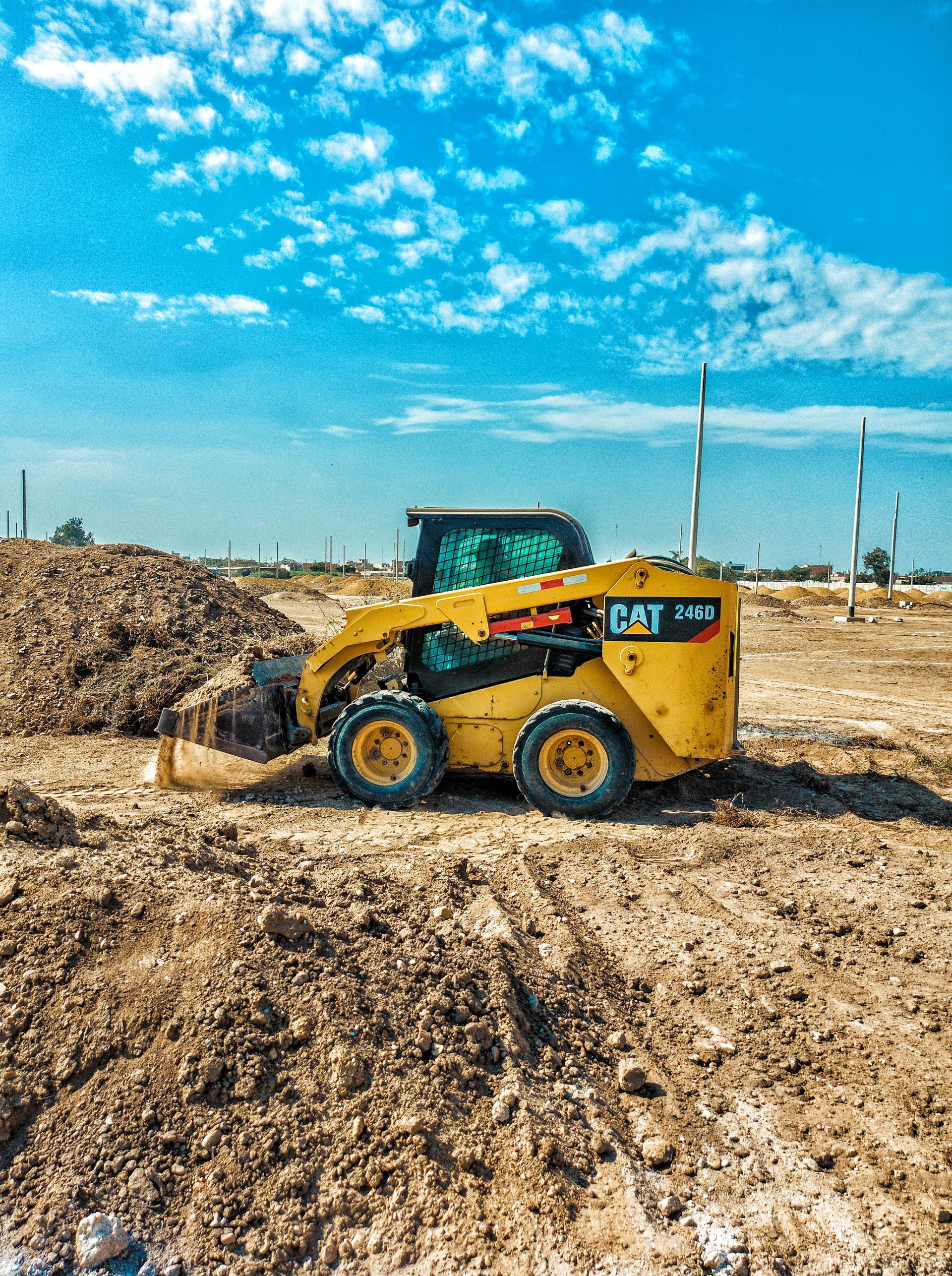Yellow skid-steer loader pushing dirt at a construction site under a blue sky