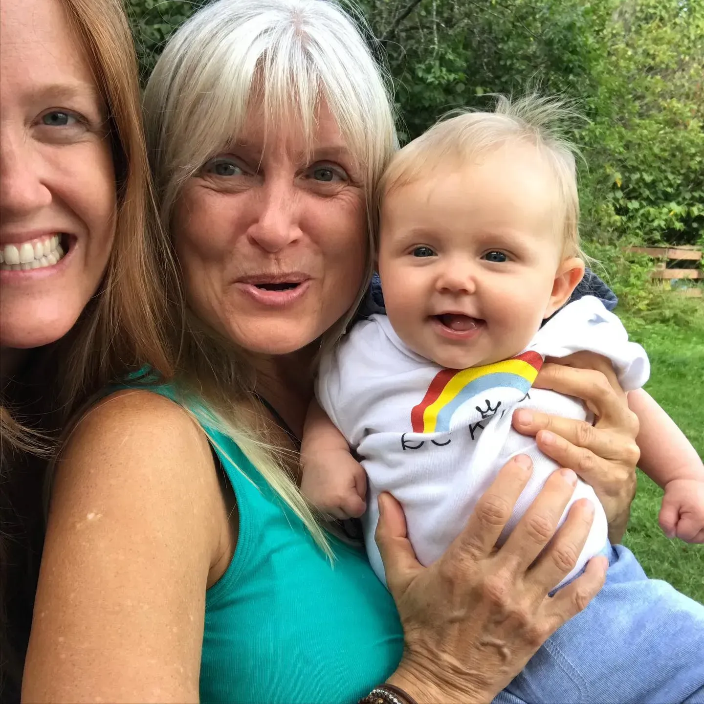 Smiling woman holding a baby outdoors, with another smiling woman partly visible beside them.
