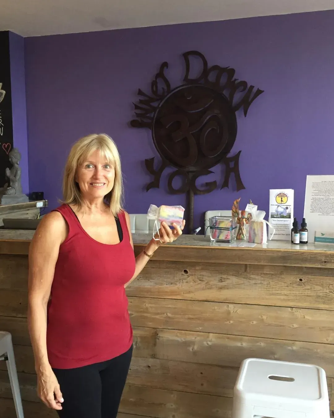Woman in a red top standing by a rustic counter in a purple-walled room, holding a small item.