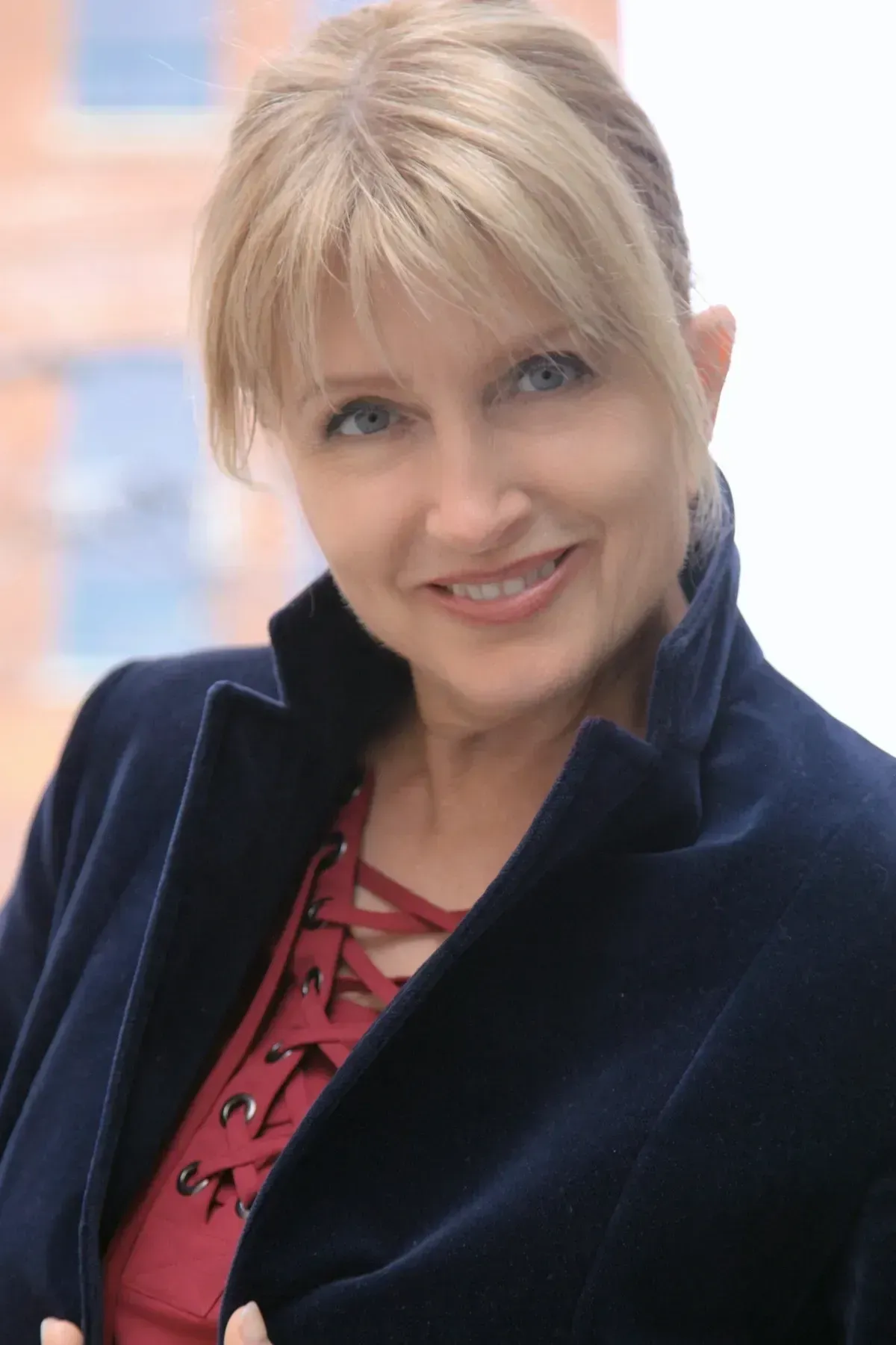Smiling woman in a navy jacket over a red top, posing against a softly blurred background