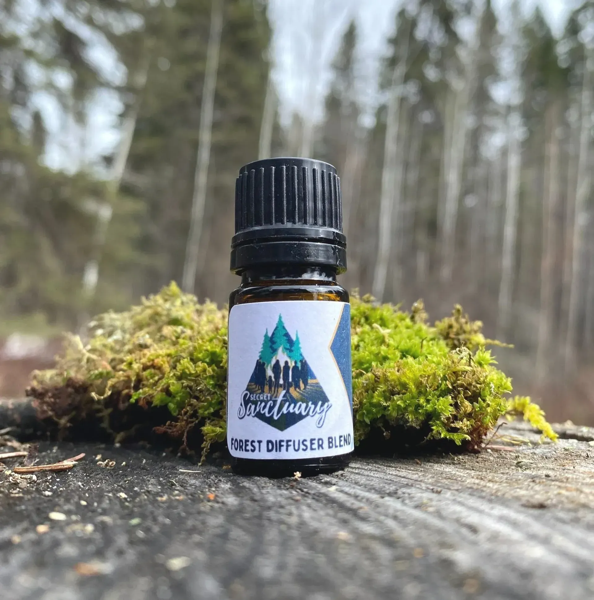 Small essential oil bottle with forest label on a mossy log in a wooded outdoor setting