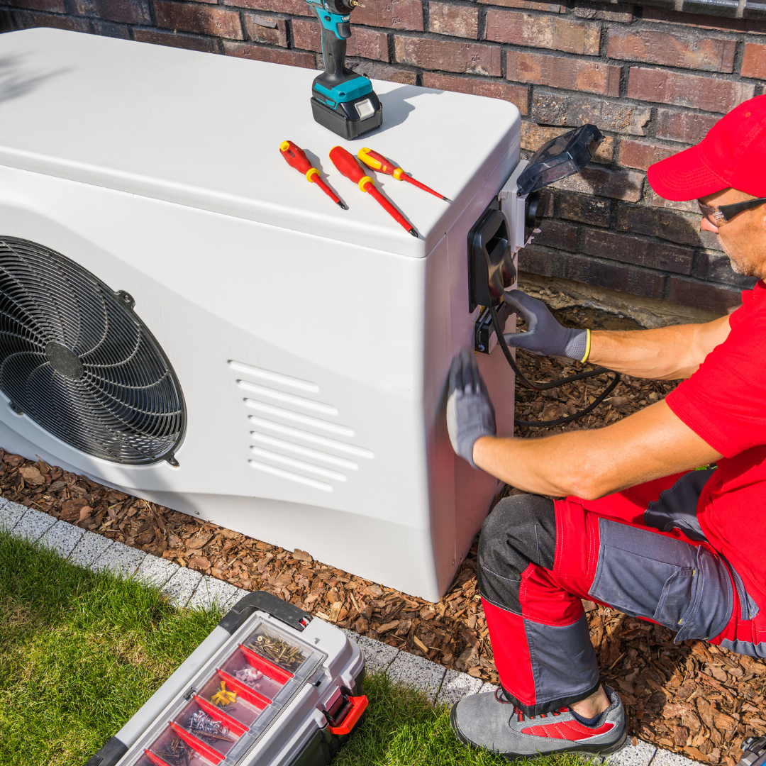 A man is working on an air conditioner outside of a house.