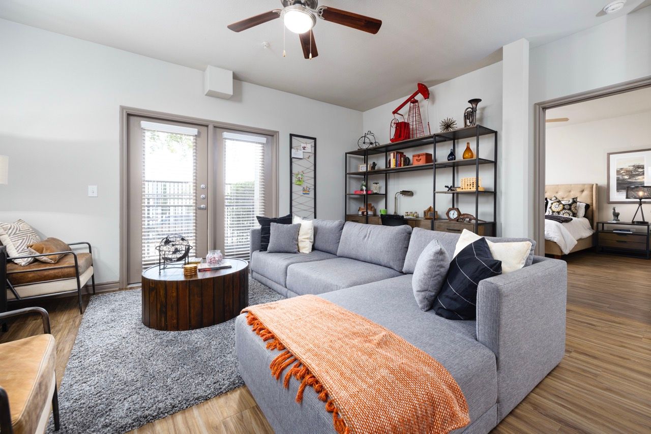 Living room of an apartment with a gray sectional sofa, round wooden coffee table, and open shelving.