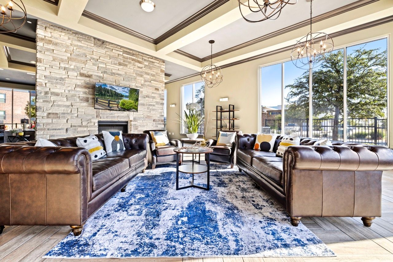 Bright community lounge with leather sofas, a stone fireplace, and large windows.