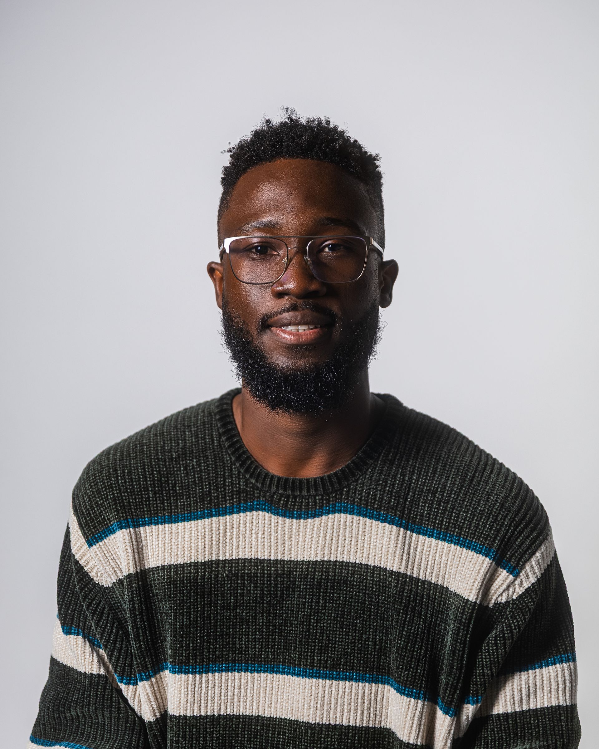 Un homme portant des lunettes et un polo noir sourit. Fond clair.