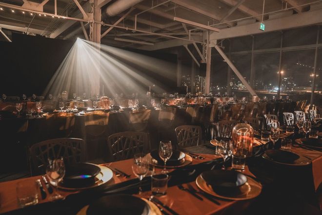 Dîner formel, tables dressées, éclairées par un projecteur, vue de la ville en arrière-plan.